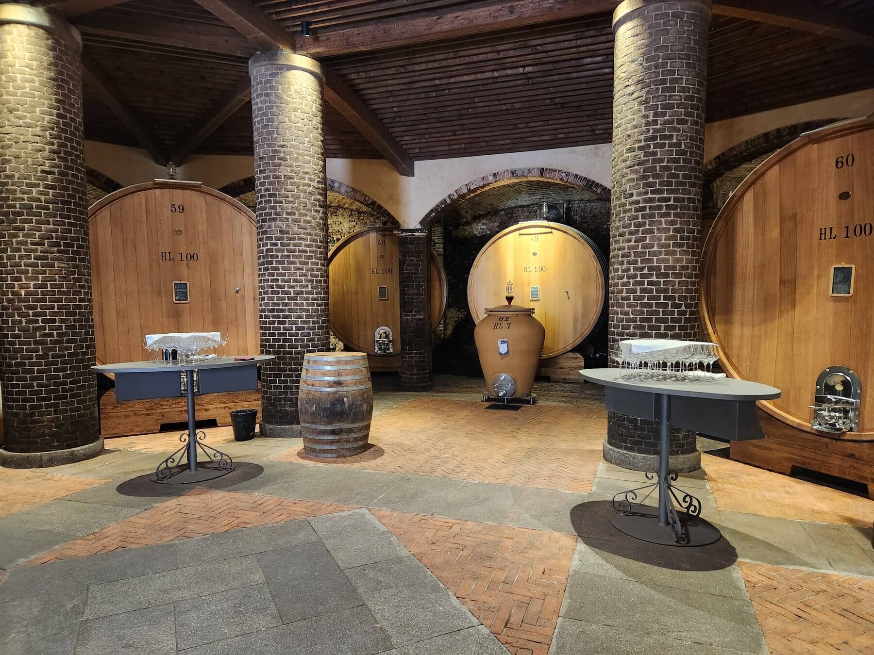 Salle de dégustation avec foudres, amphores et tables hautes dans une cave du Piémont
