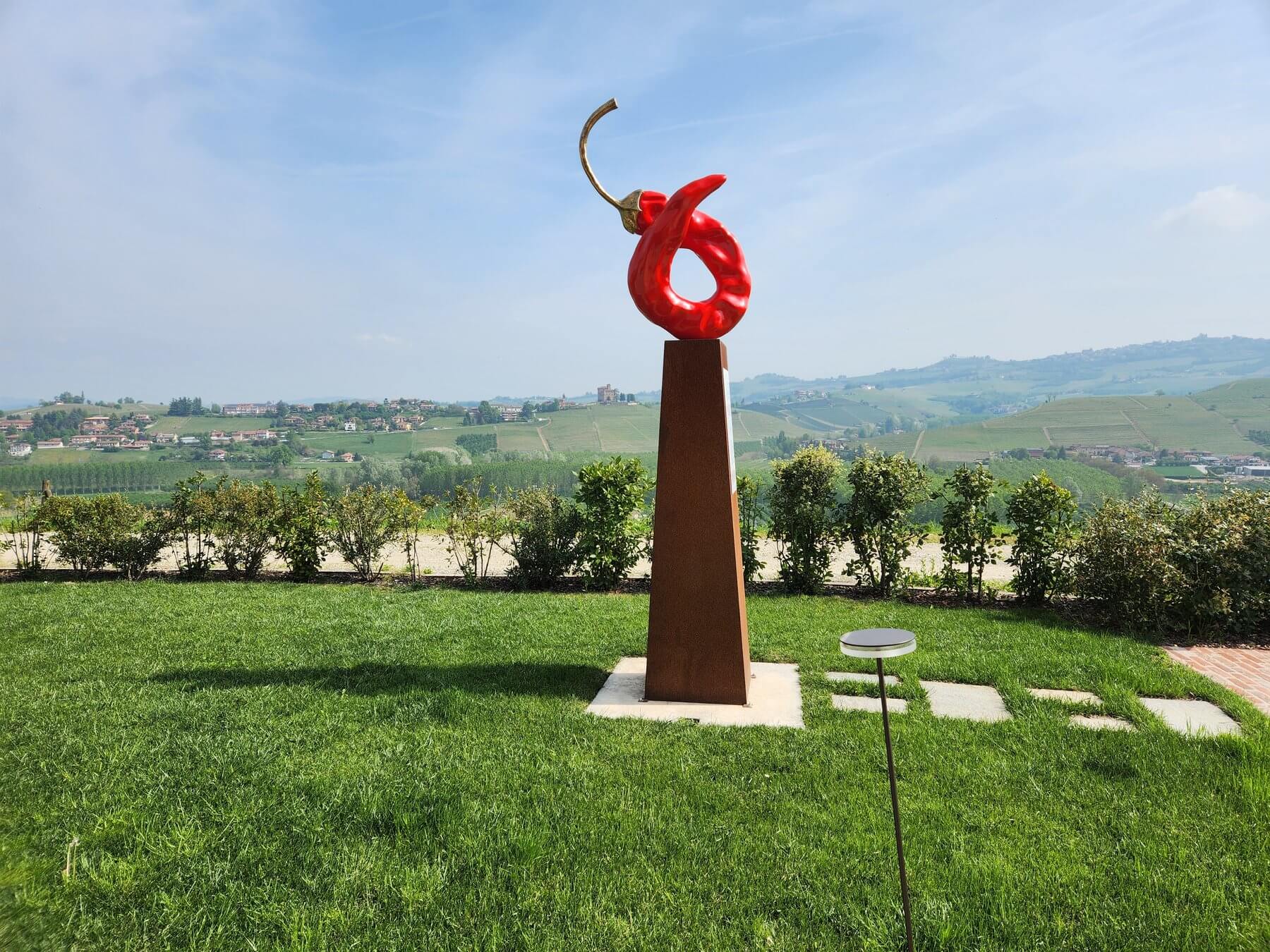 Sculpture piment rouge sur socle corten avec panorama des Langhe, domaine viticole du Piémont